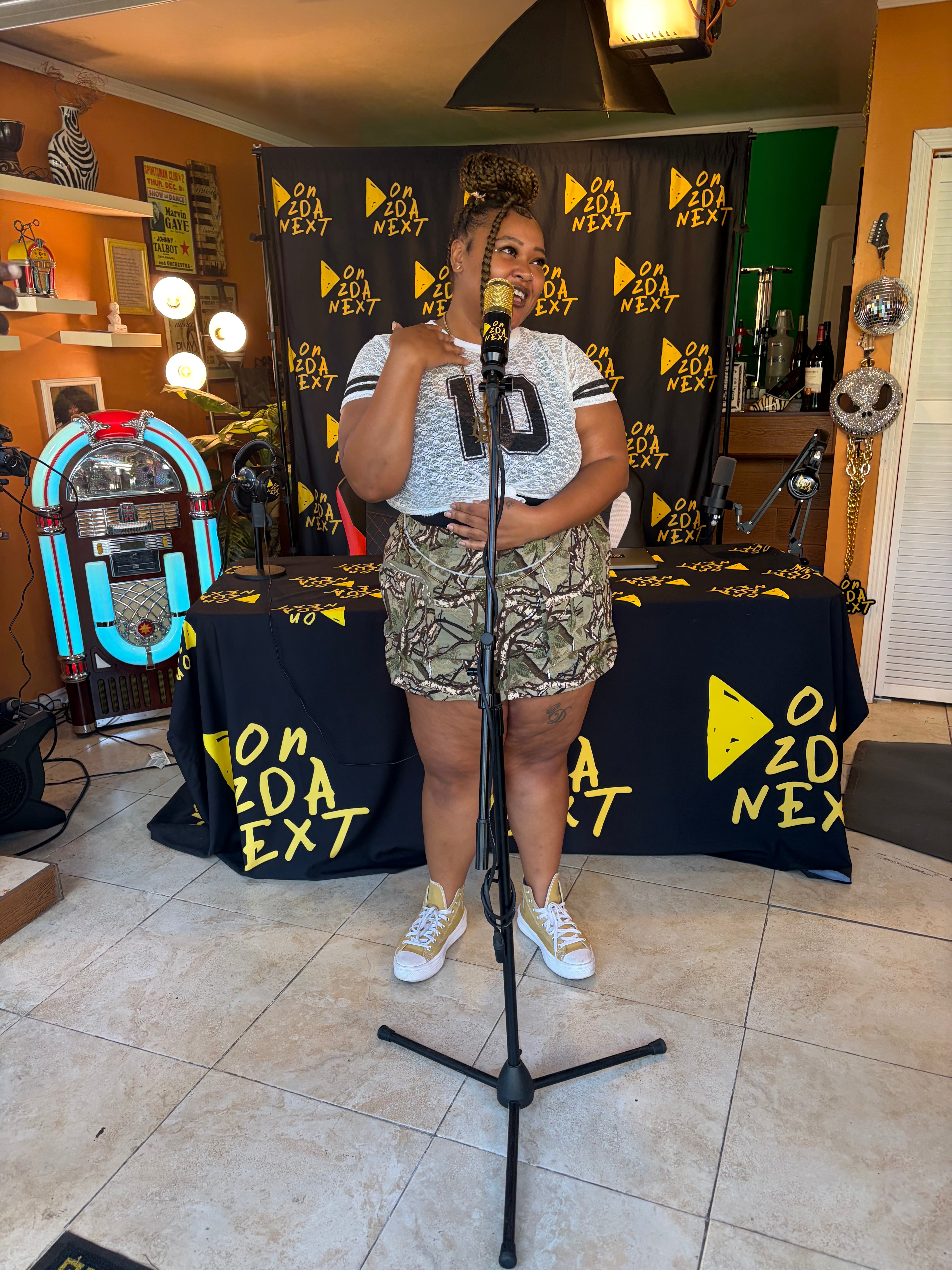 Person standing in front of a microphone with 'On Da Next' branding in the background
